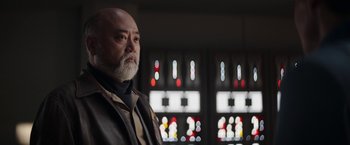 Movie still from “The Mandalorian” (2019), created by Jon Favreau – An older man with a beard standing in front of stained - glass windows; Close Up shot, Low angle