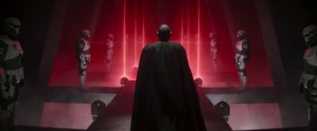 Movie still from “The Mandalorian” (2019), created by Jon Favreau – A man in a black cape standing in front of a red background; Wide shot, Low angle