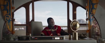 Movie still from “The Mandalorian” (2019), created by Jon Favreau – A man sitting at a desk in front of a computer monitor; Medium shot, Low angle