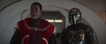 Movie still from “The Mandalorian” (2019), created by Jon Favreau – A man in a red and black outfit and a man in a black and red outfit; Medium shot, Over the shoulder angle