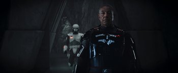 Movie still from “The Mandalorian” (2019), created by Jon Favreau – A man standing next to another man in a dark room; Medium shot, Over the shoulder angle