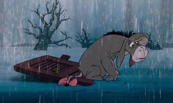Movie still from “The Many Adventures of Winnie the Pooh” (1977), directed by John Lounsbery – An eeyore sitting on the ground in the rain; Medium shot, High angle