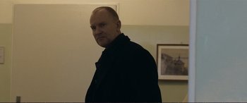 Movie still from “The Marco Effect” (2021), directed by Martin Zandvliet – A man standing in a room next to a picture; Medium shot, Over the shoulder angle
