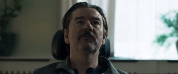 Movie still from “The Marco Effect” (2021), directed by Martin Zandvliet – A person sitting in a chair; Close Up shot, Low angle