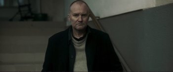 Movie still from “The Marco Effect” (2021), directed by Martin Zandvliet – A man in a black jacket is standing in front of a staircase; Medium shot, Low angle