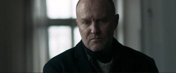 Movie still from “The Marco Effect” (2021), directed by Martin Zandvliet – A man with a beard and a jacket on looking at the camera; Close Up shot, Low angle