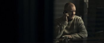 Movie still from “The Marco Effect” (2021), directed by Martin Zandvliet – A man in a sweater is talking on a cell phone; Medium shot, Over the shoulder angle
