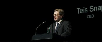 Movie still from “The Marco Effect” (2021), directed by Martin Zandvliet – A man standing at a podium speaking to a crowd; Medium shot, Low angle