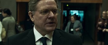 Movie still from “The Marco Effect” (2021), directed by Martin Zandvliet – A man in a suit and tie wearing glasses; Close Up shot, Over the shoulder angle