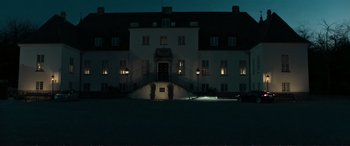 Movie still from “The Marco Effect” (2021), directed by Martin Zandvliet – A large white building lit up at night; Extreme Wide shot, Low angle