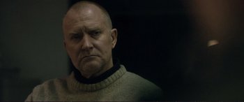 Movie still from “The Marco Effect” (2021), directed by Martin Zandvliet – An older man with a beard and a sweater on; Close Up shot, Over the shoulder angle