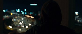 Movie still from “The Marco Effect” (2021), directed by Martin Zandvliet – A person sitting in front of a street at night; Medium shot, Over the shoulder angle