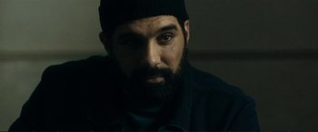 Movie still from “The Marco Effect” (2021), directed by Martin Zandvliet – A man with a beard wearing a black hat; Close Up shot, Over the shoulder angle