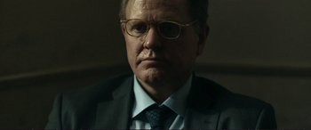 Movie still from “The Marco Effect” (2021), directed by Martin Zandvliet – A person wearing a suit and glasses; Close Up shot, Over the shoulder angle
