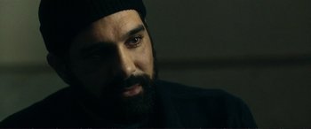 Movie still from “The Marco Effect” (2021), directed by Martin Zandvliet – A man with a beard wearing a black hat; Close Up shot, Over the shoulder angle