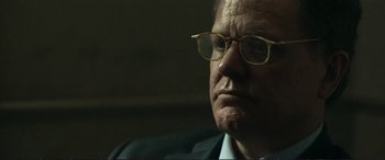 Movie still from “The Marco Effect” (2021), directed by Martin Zandvliet – An older man wearing glasses and a suit looking at the camera; Close Up shot, Over the shoulder angle
