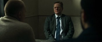 Movie still from “The Marco Effect” (2021), directed by Martin Zandvliet – A man in a suit and tie sitting at a table; Medium shot, Over the shoulder angle