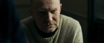 Movie still from “The Marco Effect” (2021), directed by Martin Zandvliet – An older man with a bald head wearing a sweater; Close Up shot, Over the shoulder angle