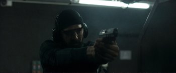 Movie still from “The Marco Effect” (2021), directed by Martin Zandvliet – A man wearing headphones and holding a gun in his hand; Close Up shot, Low angle