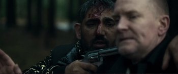 Movie still from “The Marco Effect” (2021), directed by Martin Zandvliet – A man is holding a gun with blood all over his face; Close Up shot, Over the shoulder angle