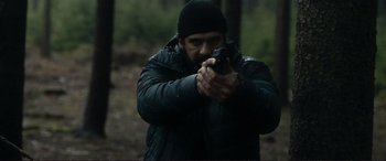 Movie still from “The Marco Effect” (2021), directed by Martin Zandvliet – A man holding a gun while standing in the woods; Medium shot, Low angle