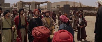 Movie still from “The Message” (1976), directed by Moustapha Akkad – A group of men standing next to each other on a dirt road; Wide shot, Over the shoulder angle