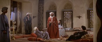 Movie still from “The Message” (1976), directed by Moustapha Akkad – A painting of a man and a woman sitting in front of an older man; Wide shot, High angle