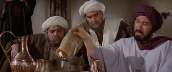 Movie still from “The Message” (1976), directed by Moustapha Akkad – Two men dressed in traditional clothing are looking at something in a jar; Medium shot, Over the shoulder angle