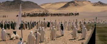 Movie still from “The Message” (1976), directed by Moustapha Akkad – A large group of people standing in the desert; Extreme Wide shot, High angle