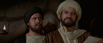 Movie still from “The Message” (1976), directed by Moustapha Akkad – A group of men standing next to each other in a room; Close Up shot, Over the shoulder angle