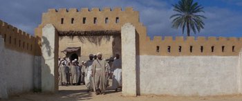 Movie still from “The Message” (1976), directed by Moustapha Akkad – A group of men in traditional clothing walking in front of a building; Wide shot, Low angle