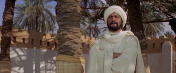 Movie still from “The Message” (1976), directed by Moustapha Akkad – A man in a turban standing next to a palm tree; Medium shot, Low angle