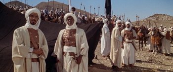 Movie still from “The Message” (1976), directed by Moustapha Akkad – A group of men in white robes standing next to each other on a beach; Wide shot, Low angle