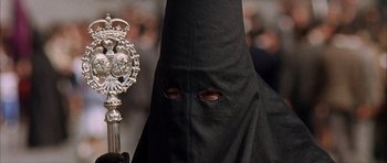 Movie still from “The Moment of Truth” (1965), directed by Francesco Rosi – A man in a black hooded robe holding a silver scepter; Close Up shot, High angle