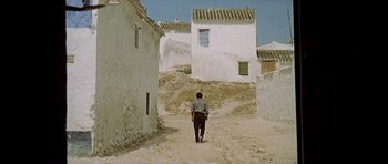 Movie still from “The Moment of Truth” (1965), directed by Francesco Rosi – A man walking down a dirt road near a row of houses; Extreme Wide shot, Low angle