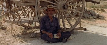 Movie still from “The Moment of Truth” (1965), directed by Francesco Rosi – A man sitting on the ground next to a wagon wheel; Wide shot, High angle