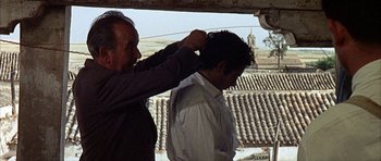 Movie still from “The Moment of Truth” (1965), directed by Francesco Rosi – A man is fixing another man's hair on a roof; Medium shot, Over the shoulder angle