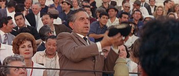 Movie still from “The Moment of Truth” (1965), directed by Francesco Rosi – A man in a brown suit is holding a microphone in front of a group of people; Medium shot, Low angle