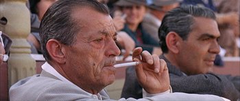 Movie still from “The Moment of Truth” (1965), directed by Francesco Rosi – An older man smoking a cigarette in front of a group of people; Close Up shot, Low angle