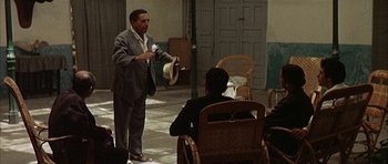 Movie still from “The Moment of Truth” (1965), directed by Francesco Rosi – A man standing in front of another man in front of a chair; Wide shot, Over the shoulder angle