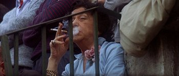 Movie still from “The Moment of Truth” (1965), directed by Francesco Rosi – An older woman smoking a cigarette while sitting in a crowd; Close Up shot, Low angle