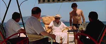 Movie still from “The Moment of Truth” (1965), directed by Francesco Rosi – A man sitting on a chair next to two other men; Medium shot, Over the shoulder angle