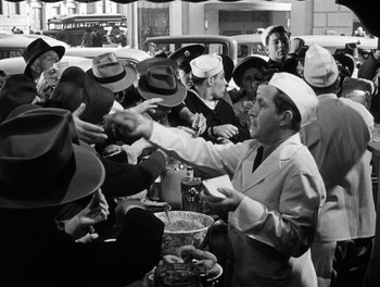 Movie still from “The More the Merrier” (1943), directed by George Stevens – A group of people standing around a table with hats on it; Medium shot, High angle