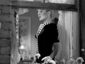 Movie still from “The More the Merrier” (1943), directed by George Stevens – A black and white photo of a woman looking out of a window; Medium shot, Low angle