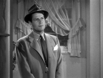 Movie still from “The More the Merrier” (1943), directed by George Stevens – A man in a suit and hat standing in front of a window; Medium shot, Low angle