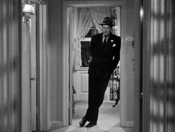 Movie still from “The More the Merrier” (1943), directed by George Stevens – A black and white photo of a man in a suit and hat; Wide shot, Low angle