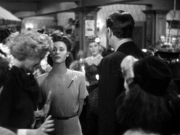Movie still from “The More the Merrier” (1943), directed by George Stevens – An old photo of a group of people in a room; Medium shot, Over the shoulder angle