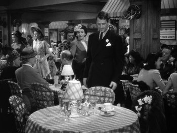 Movie still from “The More the Merrier” (1943), directed by George Stevens – A man standing in front of a table in a restaurant; Wide shot, High angle