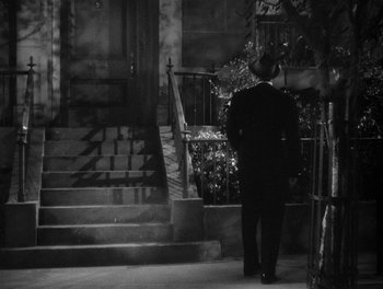 Movie still from “The More the Merrier” (1943), directed by George Stevens – A man in a suit and hat walking down the stairs of a house; Wide shot, High angle