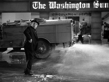 Movie still from “The More the Merrier” (1943), directed by George Stevens – A black and white photo of a man standing in front of a fire hydrant; Wide shot, Over the shoulder angle